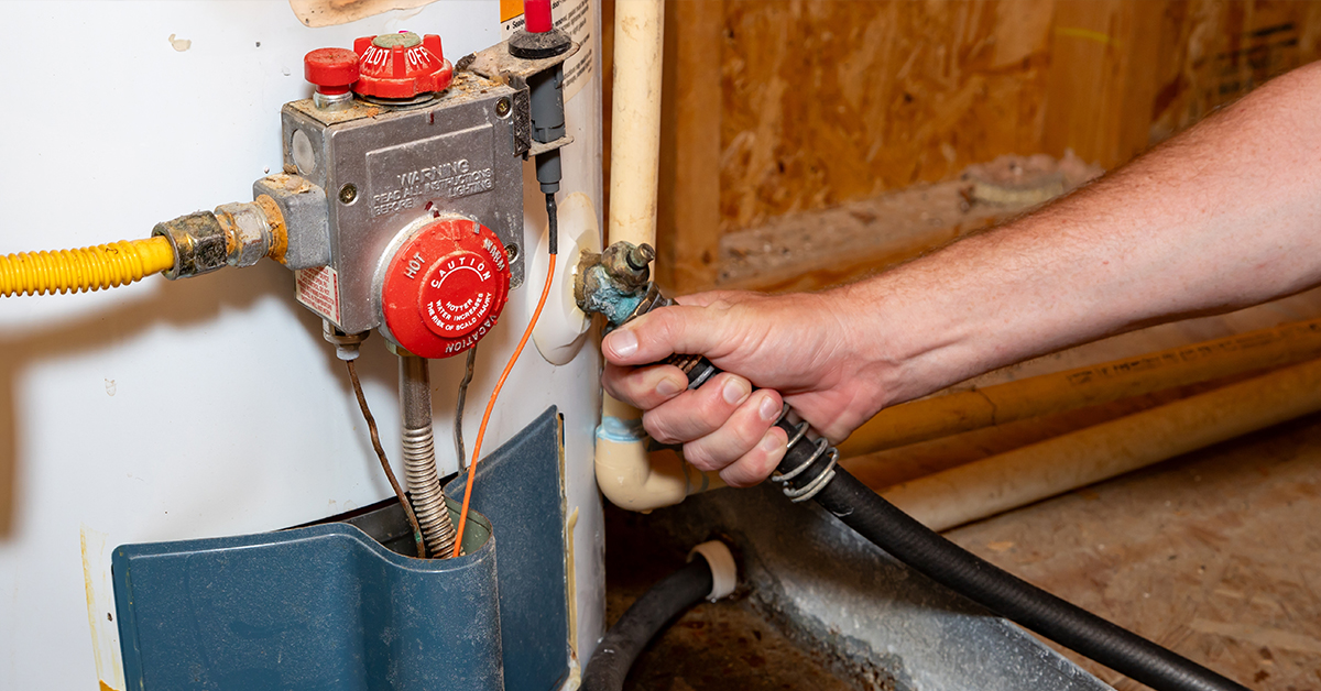 Technician connecting a drain hose to a residential gas water heater valve